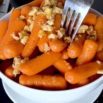 Caramelized carrots in white bowl with brown sugar and chopped nuts topping.