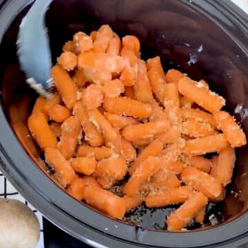 Baby carrots being mixed with a black spoon.