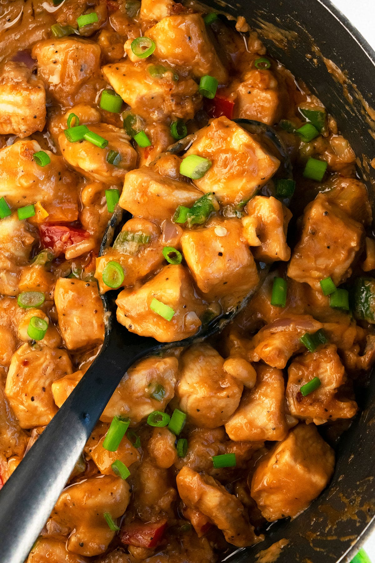 Asian Chicken Breast Cubes in Black Crockpot With Green Onion Garnish- Overhead Shot. 