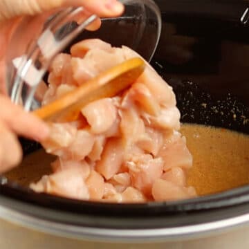 Chicken breast cubes being added to slow cooker.