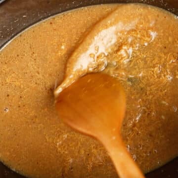 Wooden spoon being used to mix sauce until smooth. 