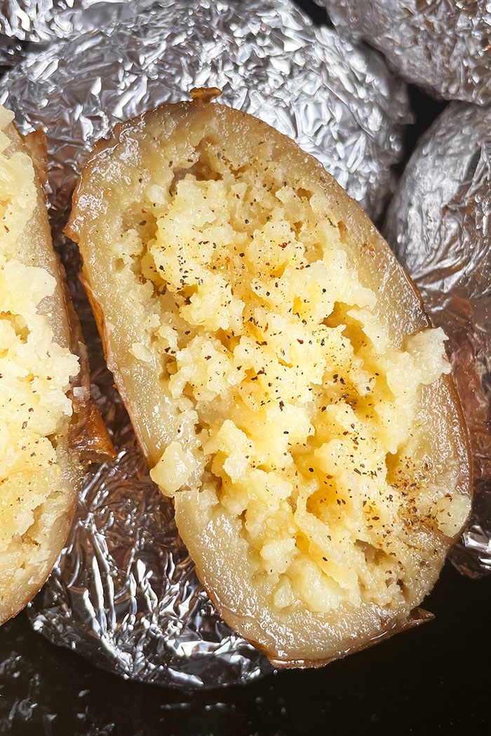 Half of a Baked Potato With Salt and Pepper Topping in Black Crockpot- Overhead Shot 