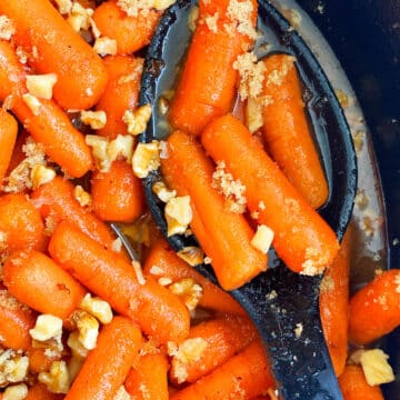 Spoonful of Homemade Glazed Carrots in Black Crockpot- Closeup Shot.