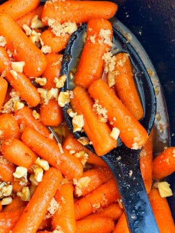Spoonful of Homemade Glazed Carrots in Black Crockpot- Closeup Shot.