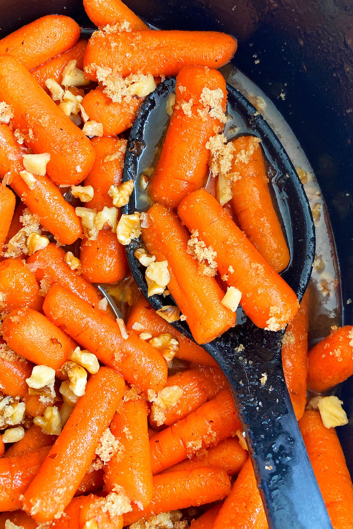 Spoonful of Homemade Glazed Carrots in Black Crockpot- Closeup Shot.