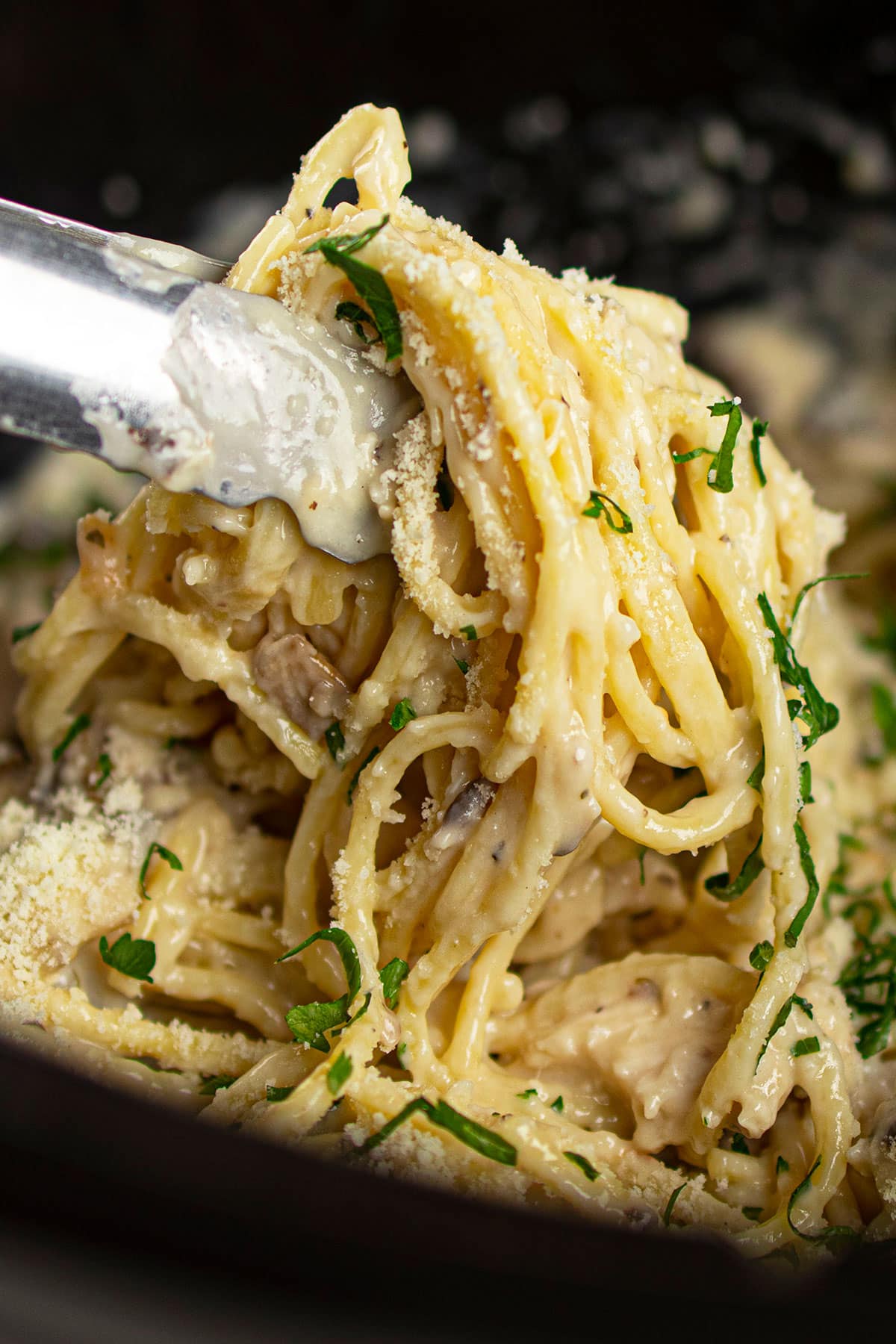 Closeup Shot of Tongs Holding Pasta Over Black Crockpot.