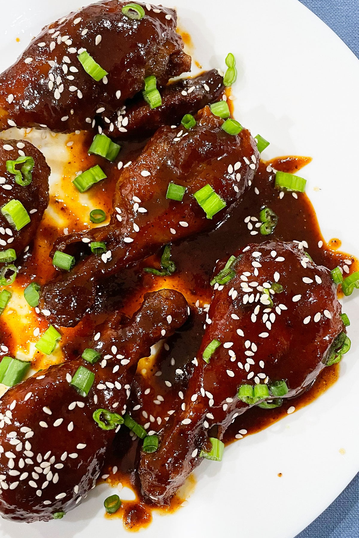 White Dish Full of Korean Chicken Topped With Sesame Seeds and Green Onions.