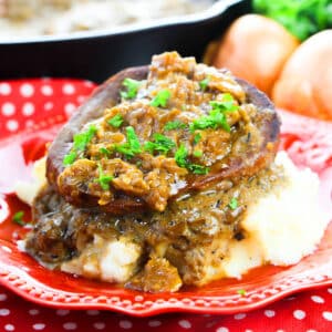Slow cooker smothered steak served over mashed potatoes in red dish.