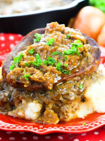 Slow cooker smothered steak served over mashed potatoes in red dish.
