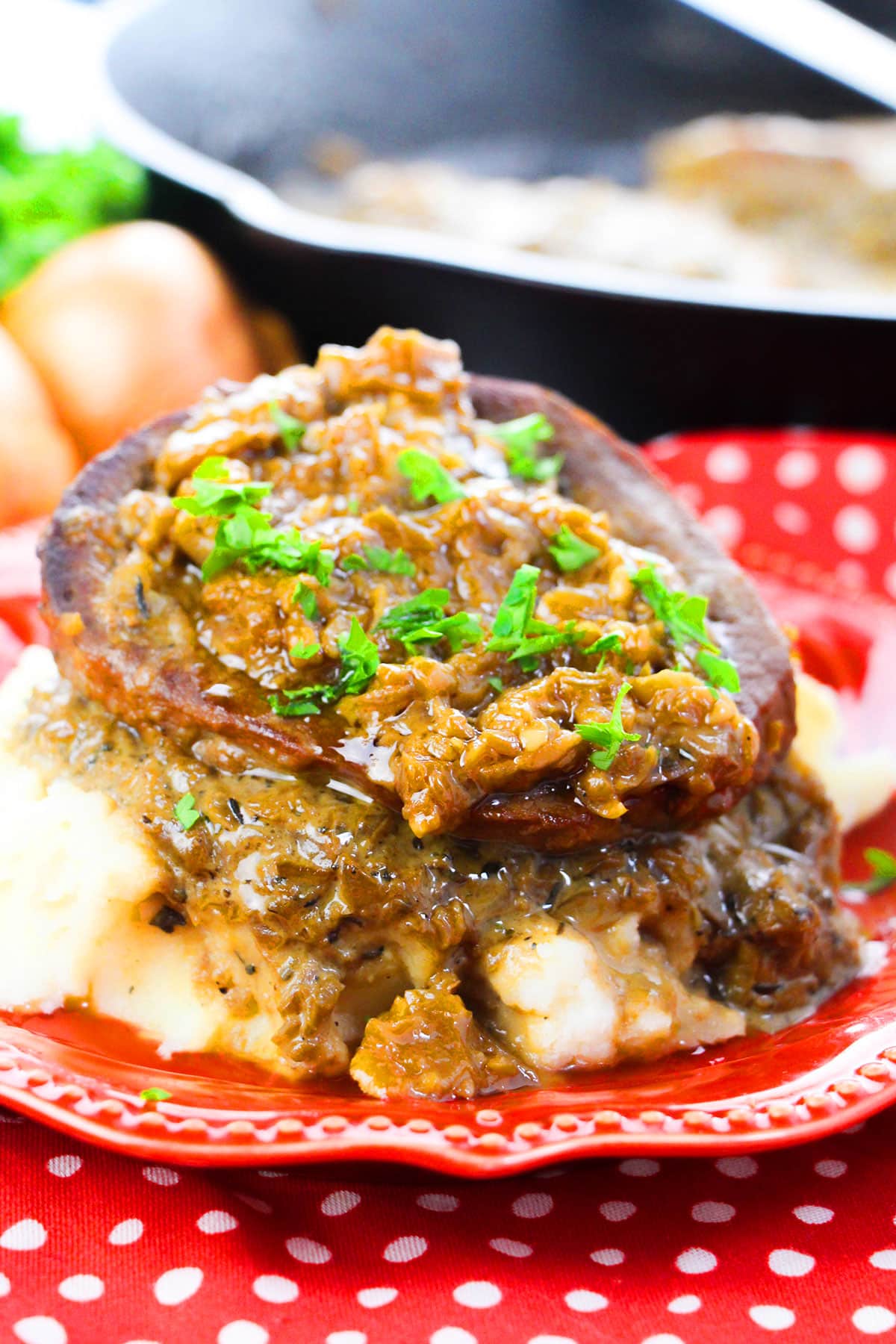 Slow cooker smothered steak with gravy served over mashed potatoes in red dish with fresh parsley garnish. 