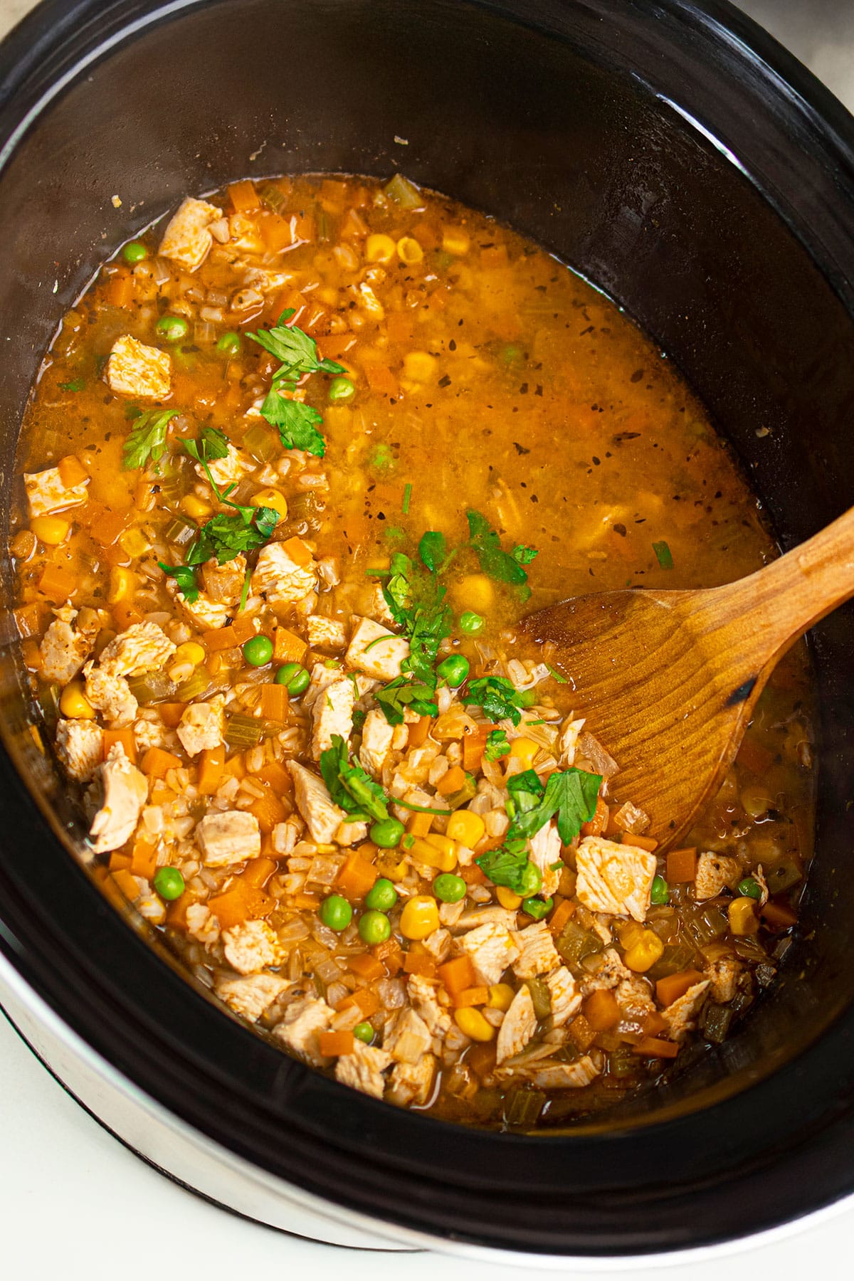 Easy Chicken and Rice Soup in Black Slow Cooker With Woden Ladle- Overhead Shot.