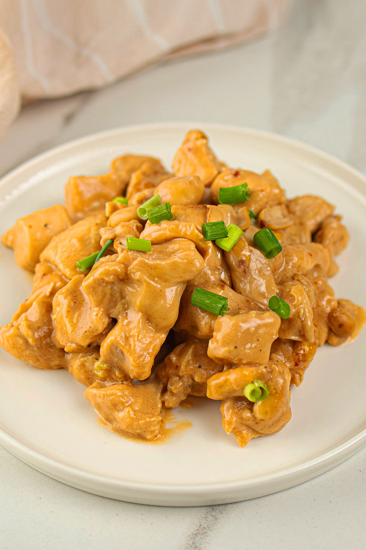 Creamy Chinese Slow Cooker Almond Chicken Garnished With Green Onions Served on White Dish.