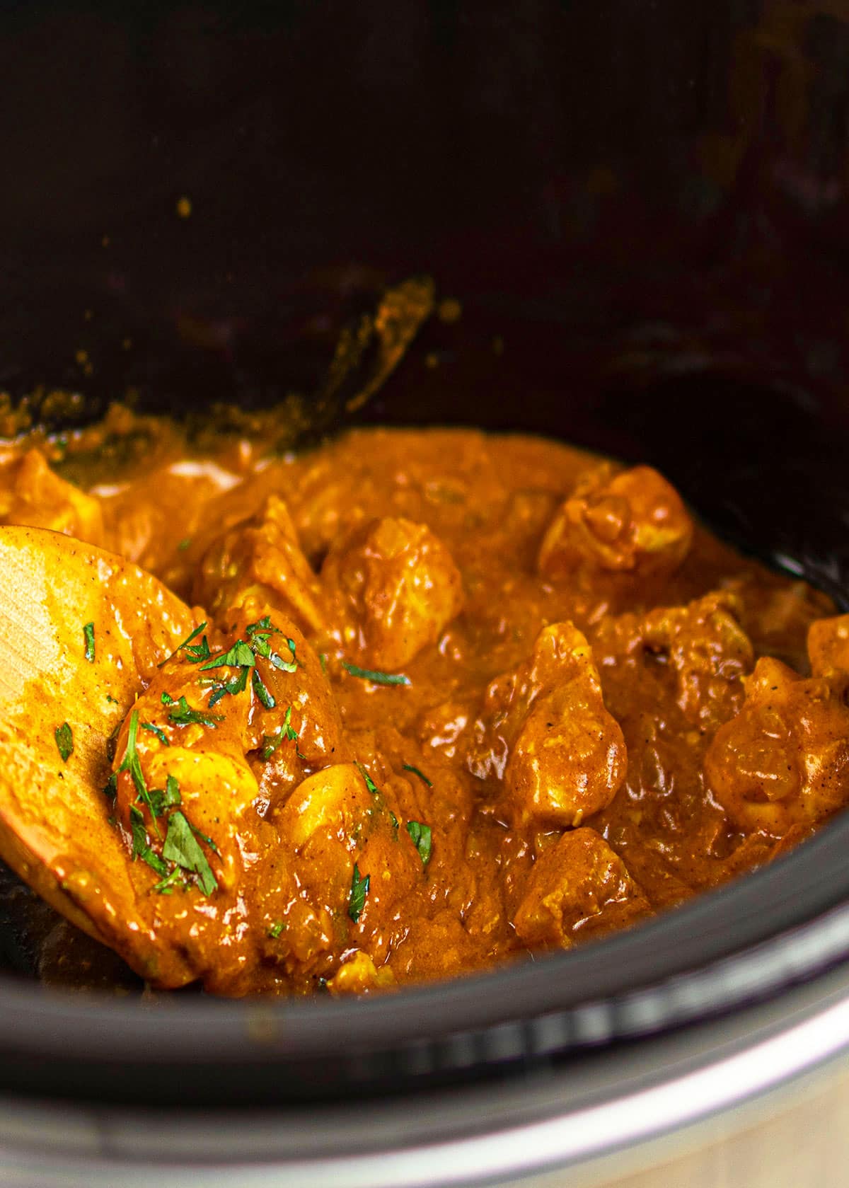 Spoonful of curry in black crockpot.