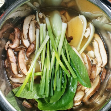 Pot with broth, mushrooms, bok choy and spring onions. 